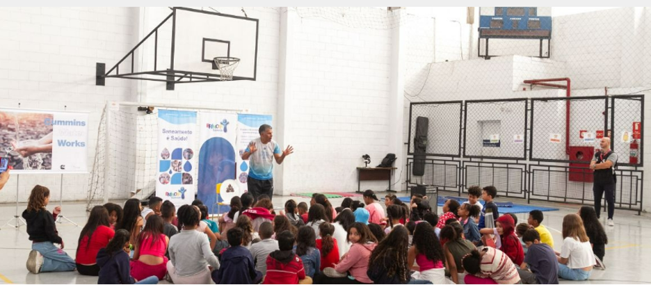 Cummins employees in Brazil participated in a project to educate students about the importance of water and sanitation. 人站在大厅给学生演示坐在前面的地板上
