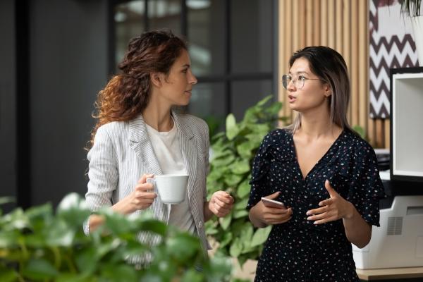Leaders play a crucial role in cultivating a culture of equity and inclusion. 两个人谈话时,一个白色的杯子在他们的手,另一个电话。在办公室的房子植物在前面和后面。