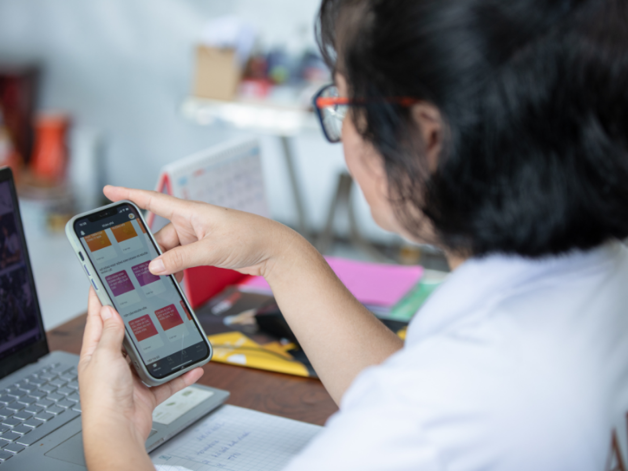Looking over a person's shoulder, they are using the HerVenture app on a cell phone. A laptop open in front of them on a desk.