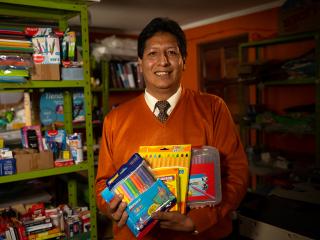 Fernando holding art supplies. Shelves of art and office supplies behind him.